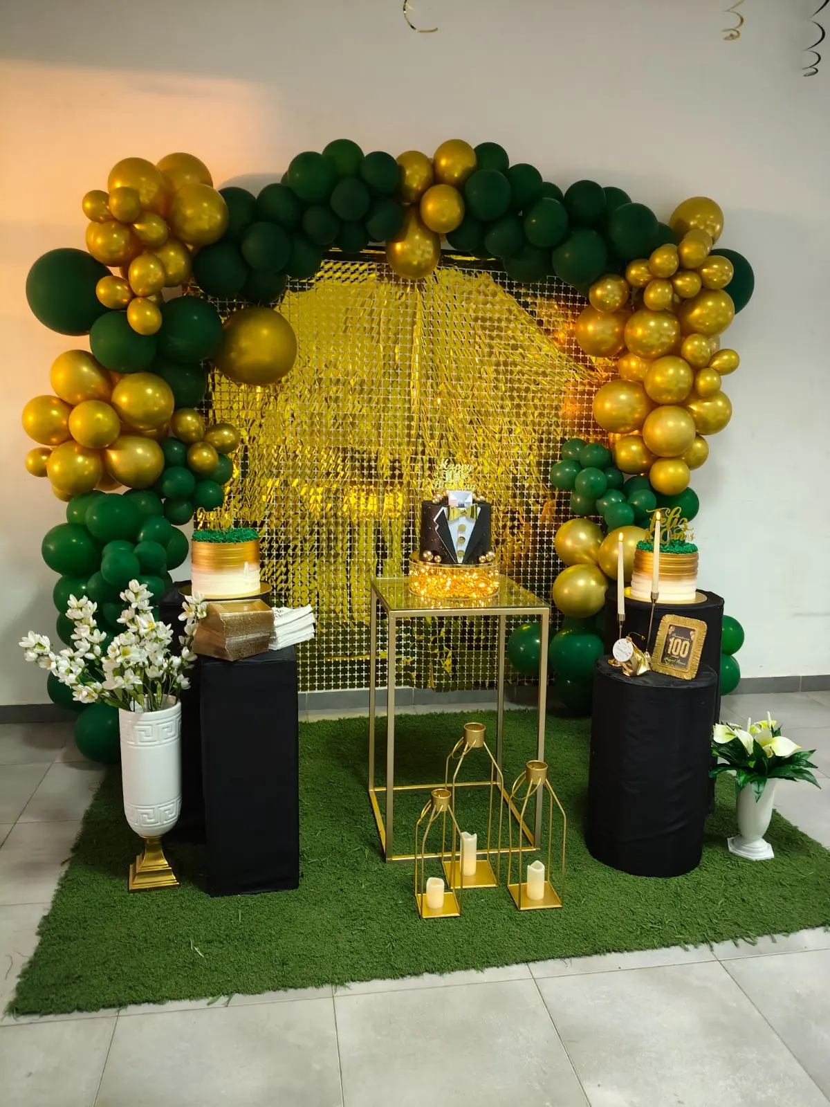 Decoração de 100.º aniversário em tons de verde e dourado, com arco de balões e bolo em formato de smoking. Espargos, Ilha do Sal, Cabo Verde.