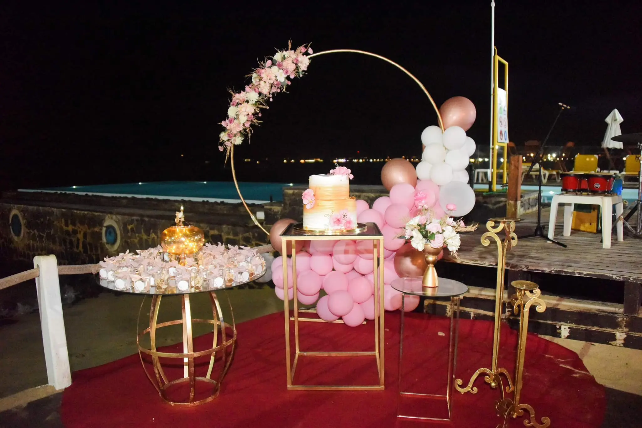 Decoração de festa noturna à beira-mar com arco dourado, balões cor-de-rosa e bolo de andares em Santa Maria, Ilha do Sal, Cabo Verde.