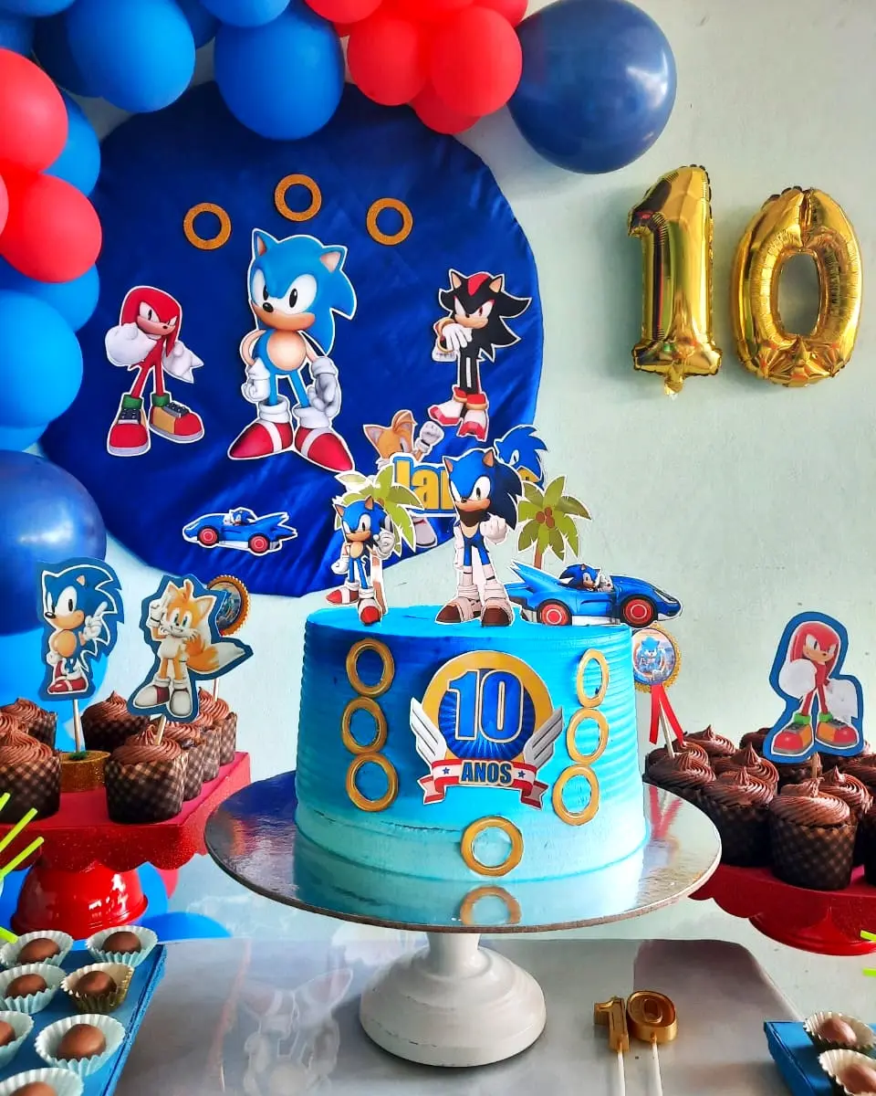 Bolo de aniversário azul com tema do Sonic e o número 10, rodeado por cupcakes de chocolate em suportes vermelhos. Espargos, Ilha do Sal, Cabo Verde.