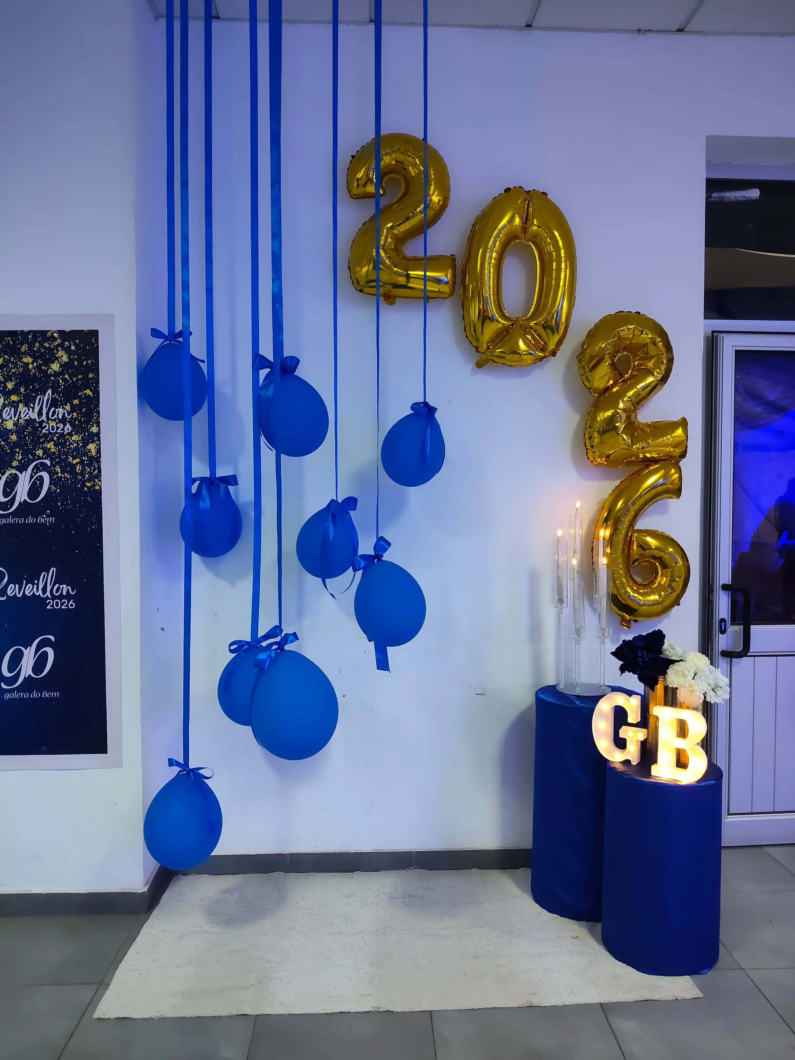 Decoração de Réveillon 2026 com balões dourados formando o ano e balões azuis suspensos. Letreiro luminoso GB em pedestais azuis. Clube ASA, Ilha do Sal, Cabo Verde.
