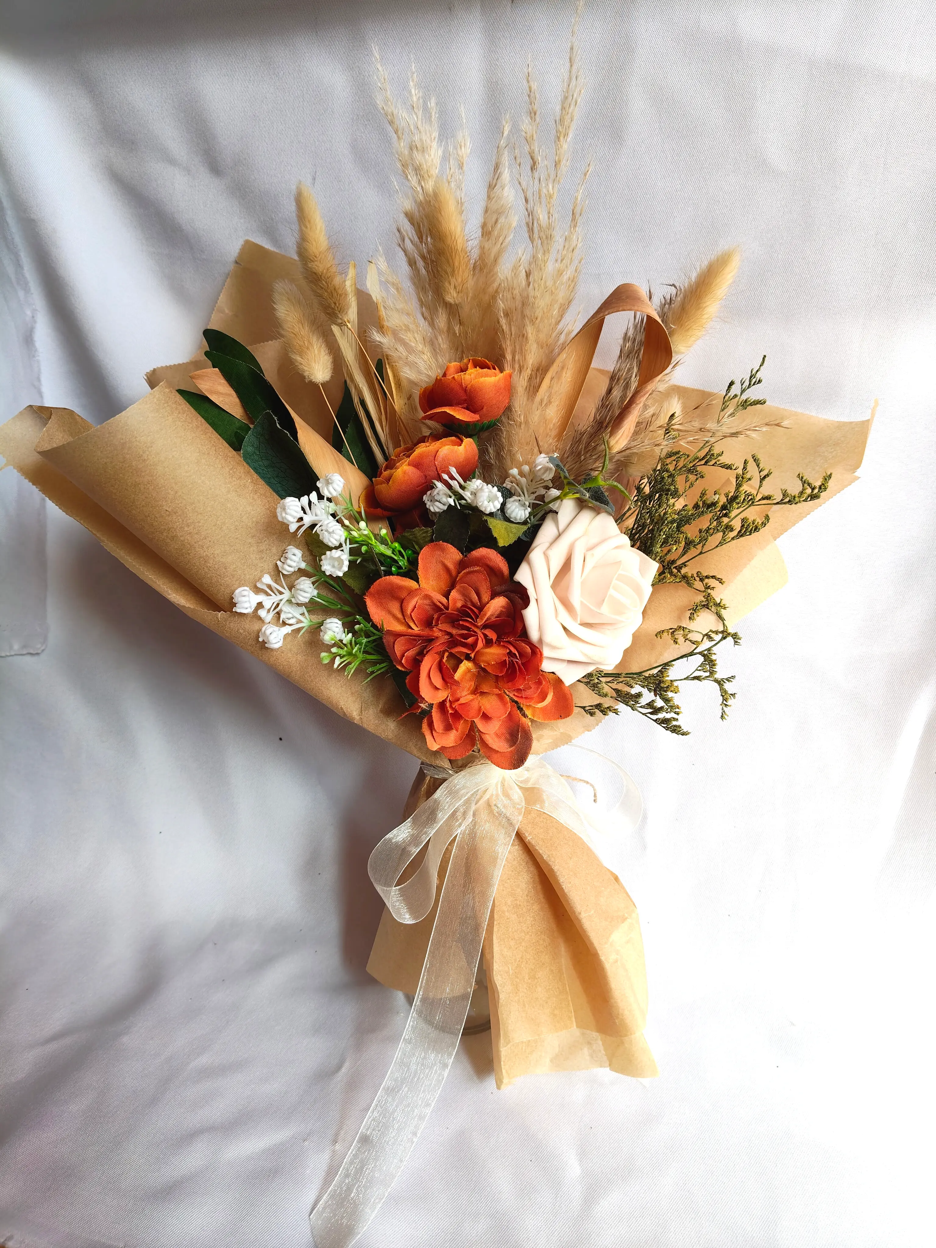 Bouquet rústico envolvido em papel kraft com flores artificiais em tons de laranja e folhagens secas. Ilha do Sal, Cabo Verde.