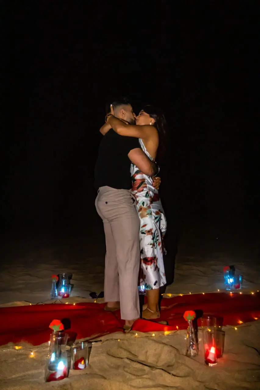 Casal a beijar-se apaixonadamente à noite na praia de Santa Maria após o pedido de casamento, sobre um tapete vermelho rodeado de velas e luzes decorativas. Ilha do Sal, Cabo Verde.