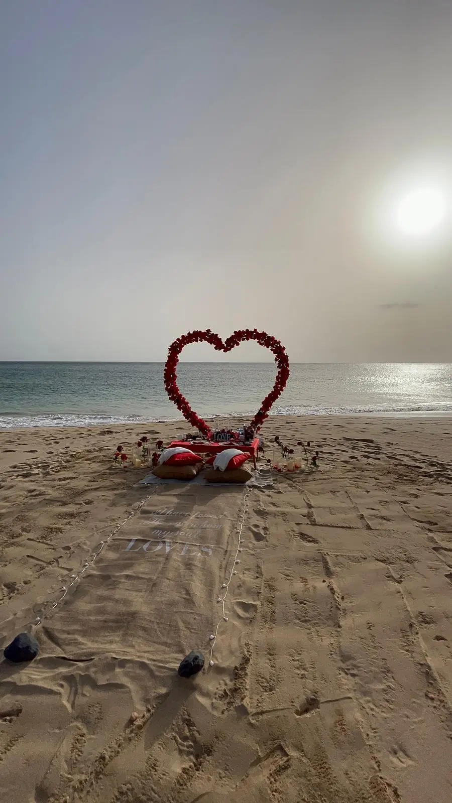 Cenário romântico na praia de Santa Maria, Ilha do Sal, com um grande coração de rosas vermelhas, pequena mesa para dois e tapete com a palavra LOVE de frente para o mar.
