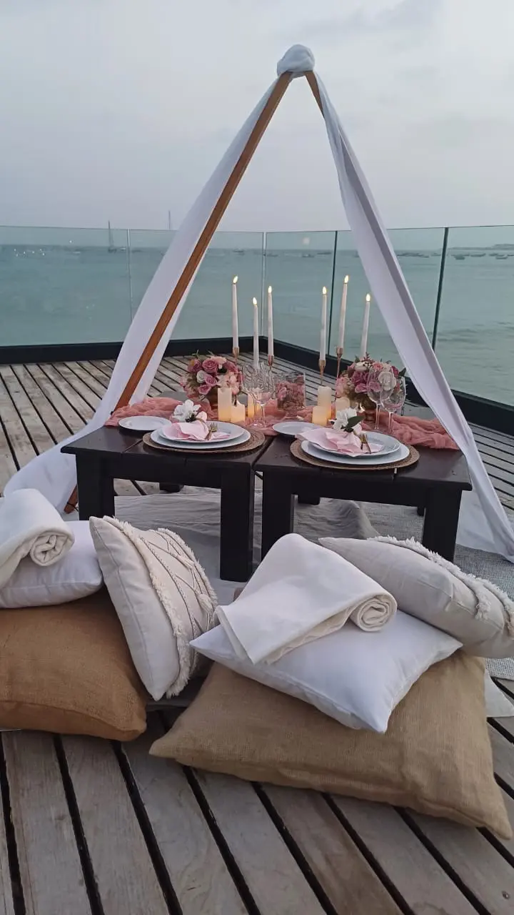 Piquenique romântico com tenda branca, mesa baixa decorada com arranjos florais cor-de-rosa, velas e almofadas confortáveis na praia de Santa Maria, Ilha do Sal, Cabo Verde.