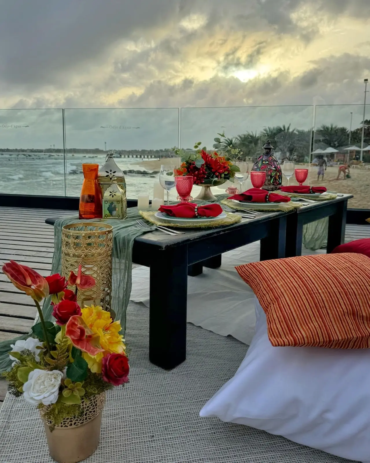 Mesa de piquenique com almofadas em tons de laranja e vermelho e vista para o mar ao pôr do sol em Santa Maria, Ilha do Sal, Cabo Verde.