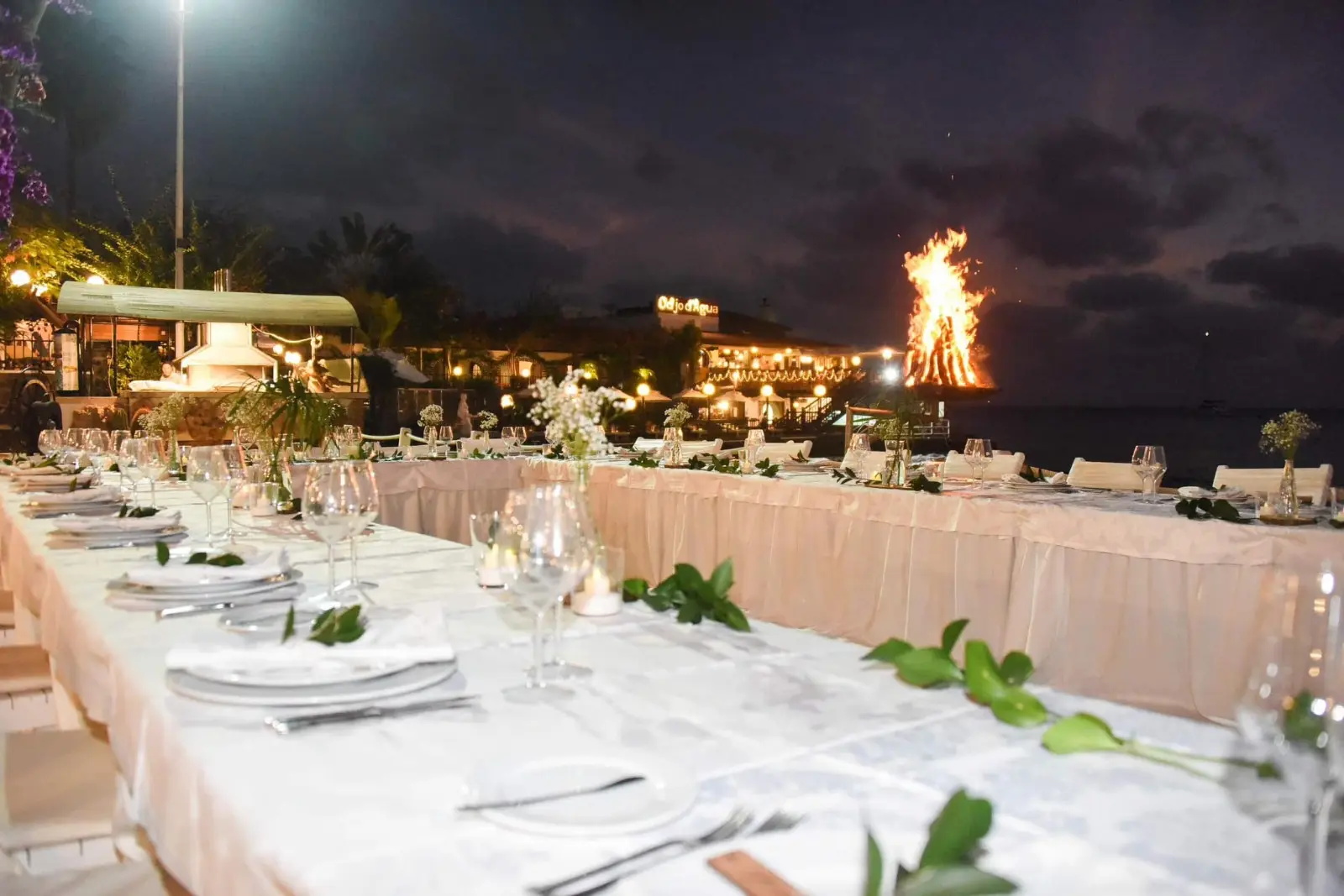 Decoração de jantar de casamento à noite na praia com mesas compridas e fogueira ao fundo. Santa Maria, Ilha do Sal, Cabo Verde.